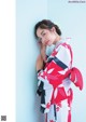 A woman in a red and white kimono leaning against a wall.